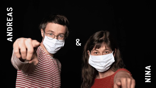 Zwei Menschen mit Hygienemasken stehen vor einem schwarzen Hintergrund und zeigen mit ihren Zeigefingern in die Kamera. Links steht Andreas, rechts Nina. Die Namen sind mit weiß auf das Bild geschrieben. Zwischen ihnen ist ein &-Zeichen