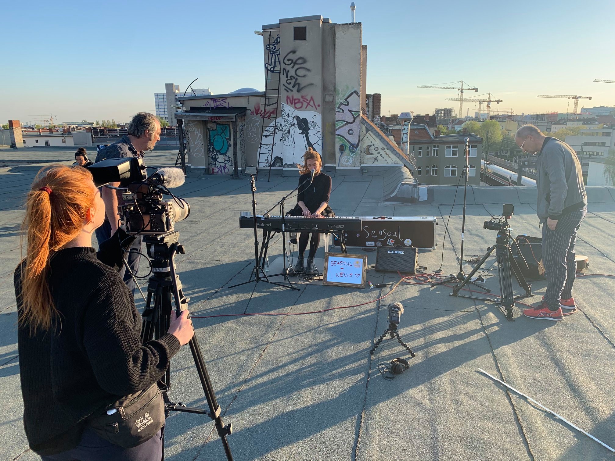 Eine Künstlerin sitzt am Keyboard auf dem Dach des Quartiersmanagement. Drum herum sieht man das Kamerateam, die Sonne steht tief und gibt ein schönes Ambiente