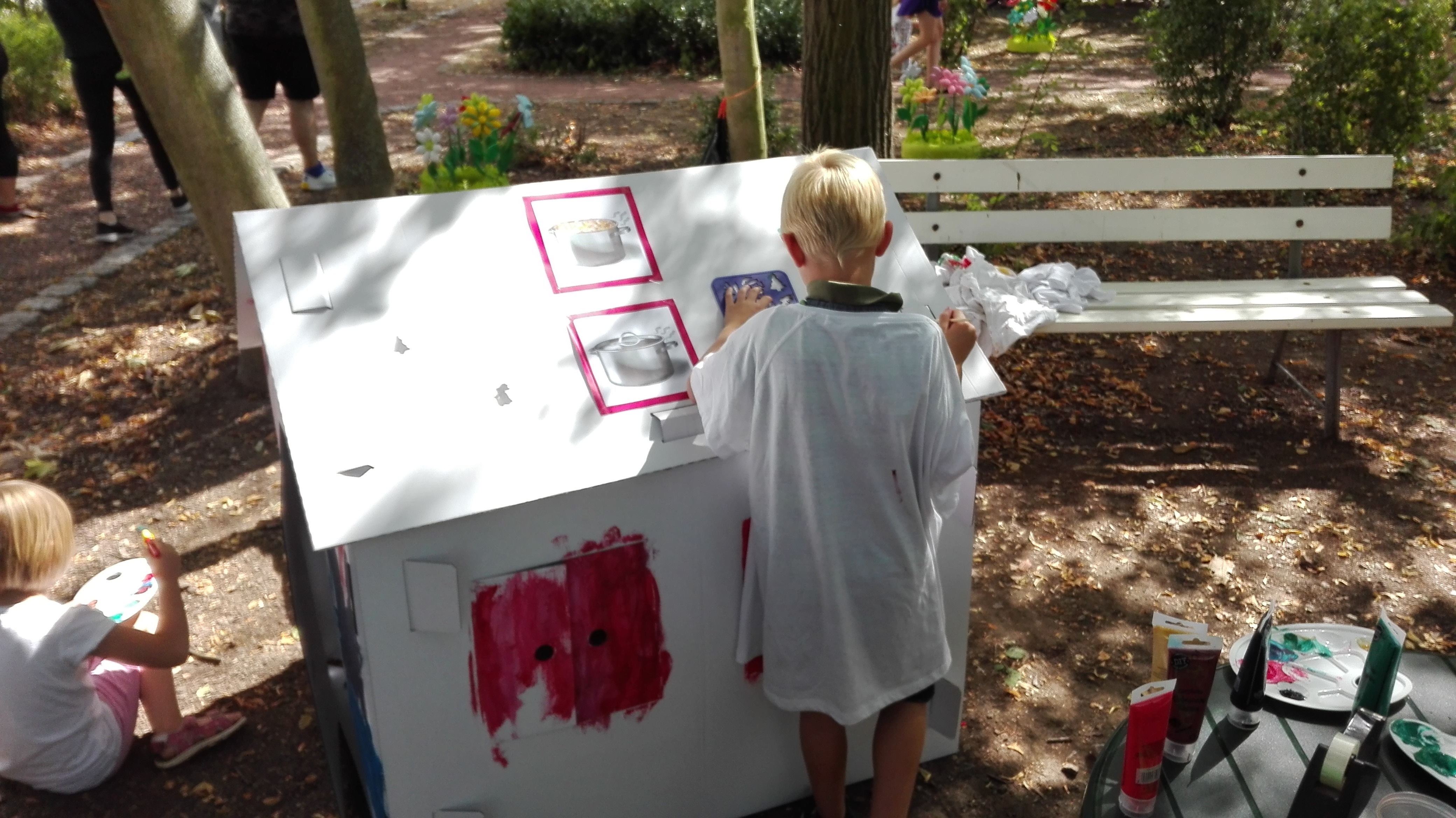 Ein Kind bemalt mit Farbe ein weißes Papphaus. 