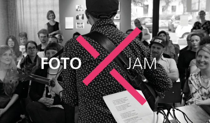 Sänger mit Gitarre, von hinten fotografiert. Hinter ihm sieht man das Publikum. Das Logo der Veranstaltung, ein rotes X inzwischen der Namens "Foto Jam", ist darüber gelegt. Das Bild im Hintergrund ist schwarz-weiß gehalten.